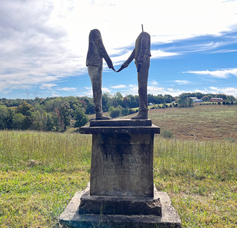 cement sculptures of two headless men shaking hands in a field