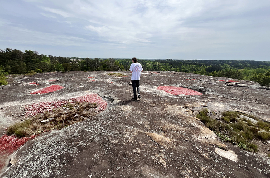 a man standing on a granite outcrop with pools of red moss