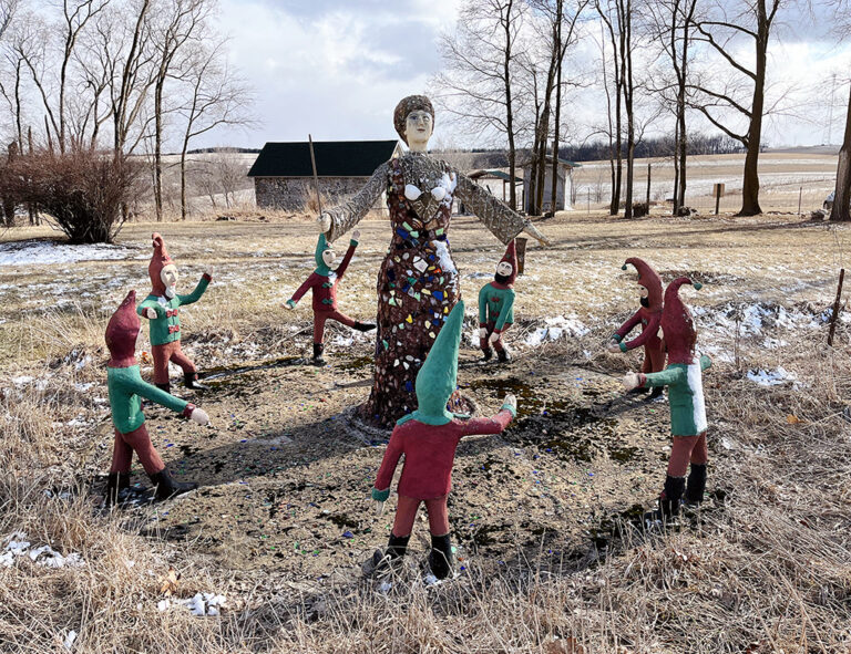 concrete sculptures of a woman surrounded by a circle of dwarves