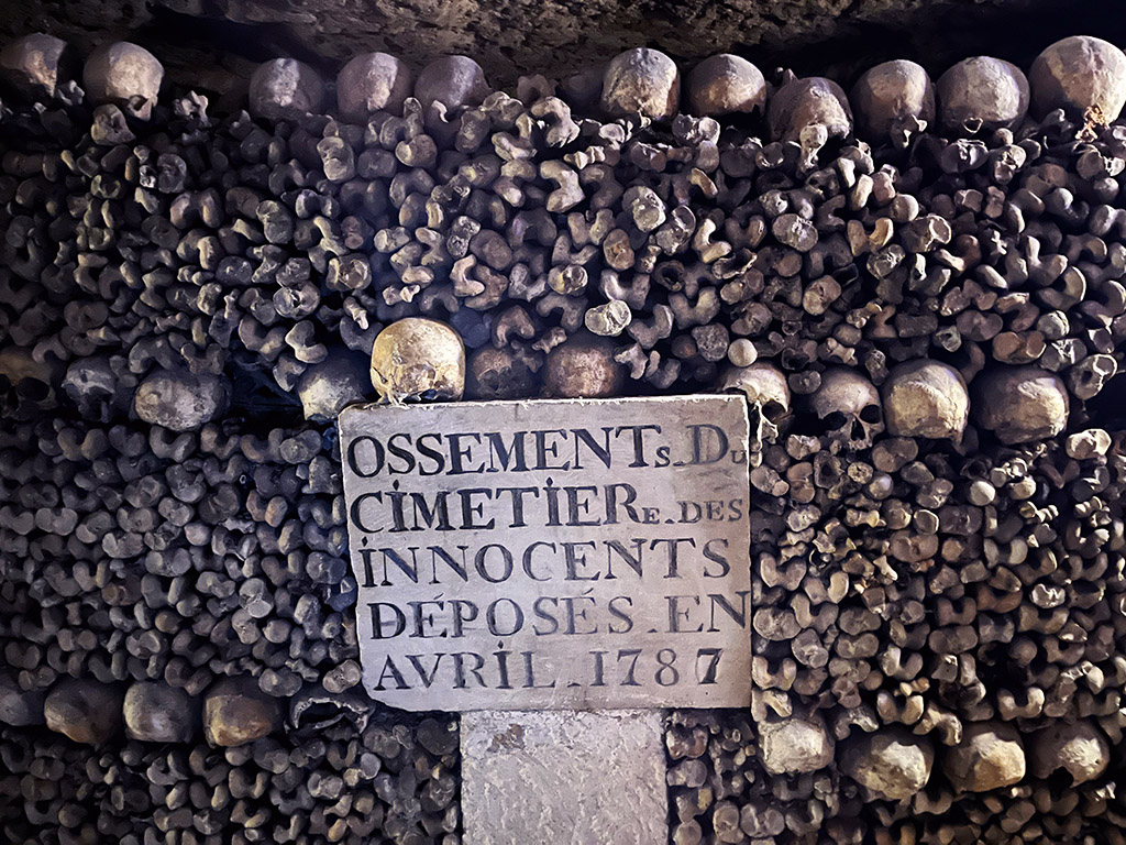 a stone plaque surrounded by neatly stacked bones in the Paris catacombs
