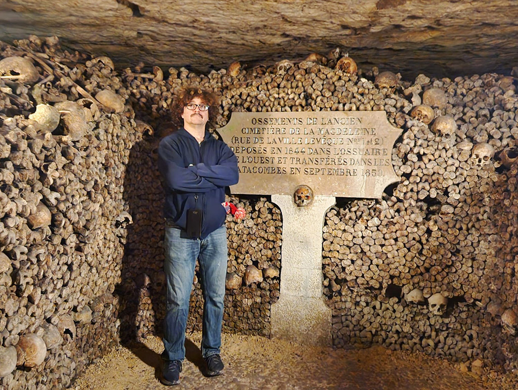 A man standing by a plaque in the Paris catacombs