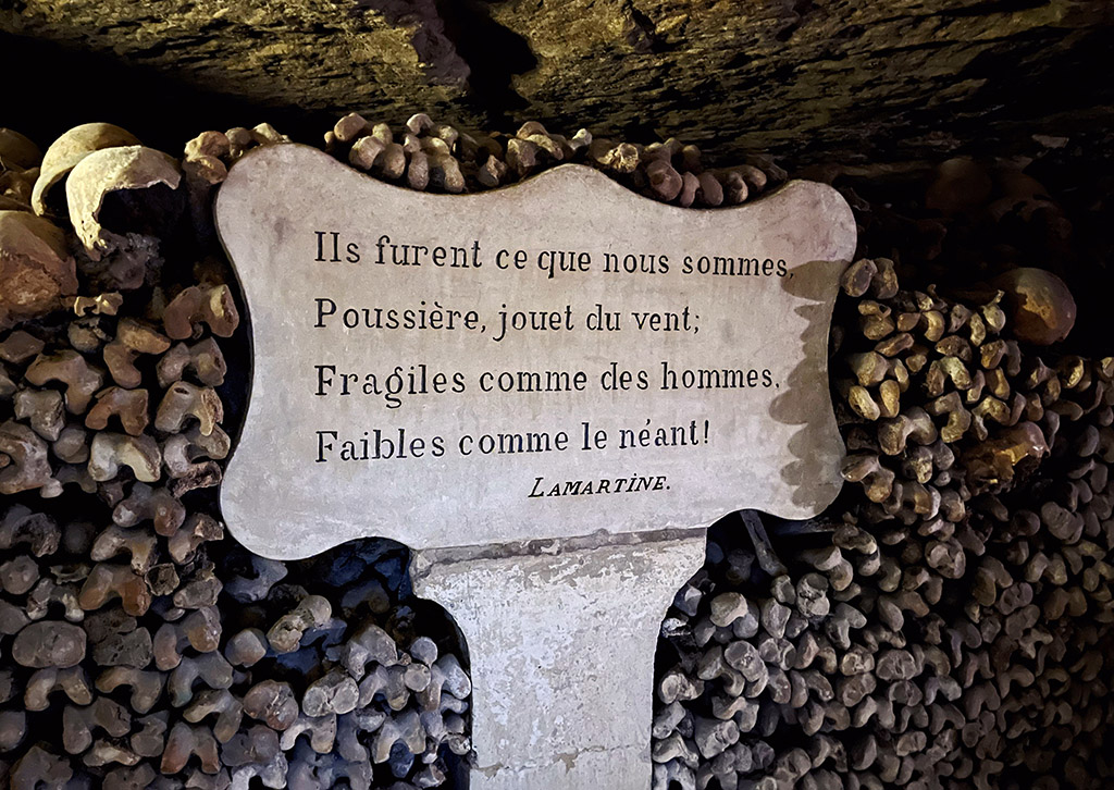 a french quote on a stone plaque in a wall of neatly stacked bones in the Paris catacombs