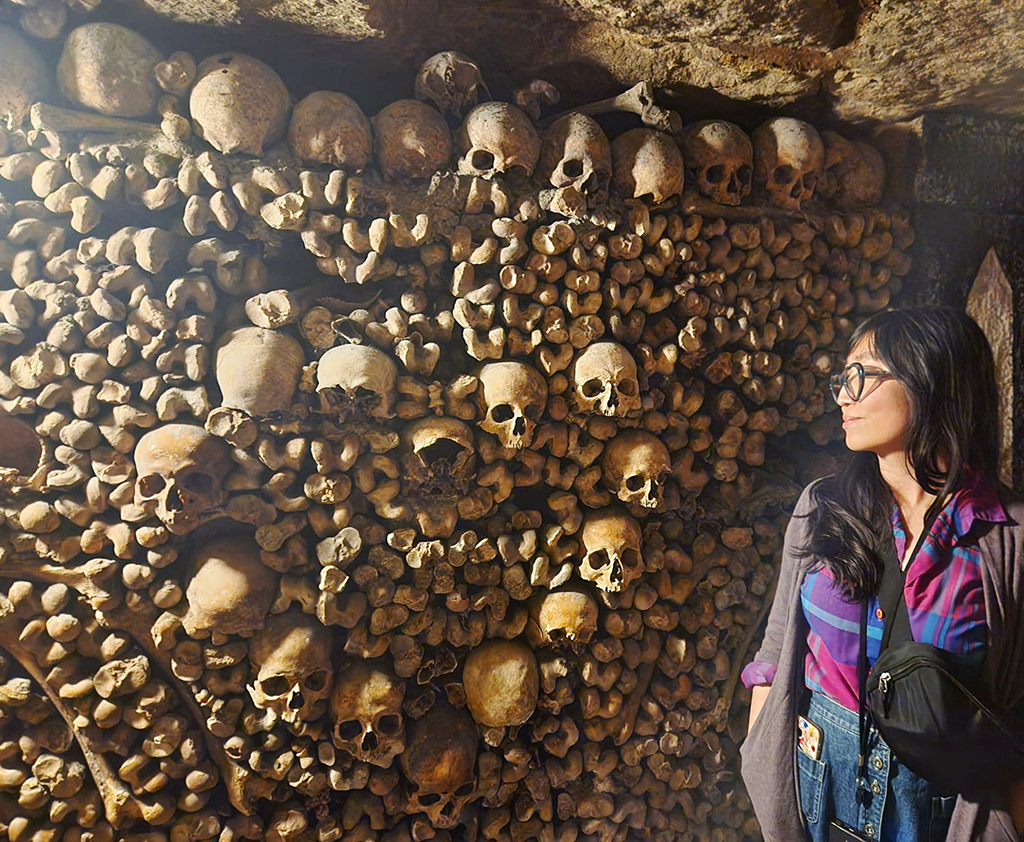 woman looking over at skulls arranged in a heart in the Paris catacombs