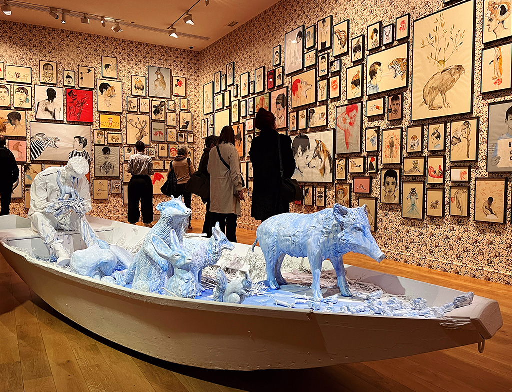 a lifesize pale blue ceramic boat with a boy crying surrounded by many animals. The walls behind the boat are covered in illustrations
