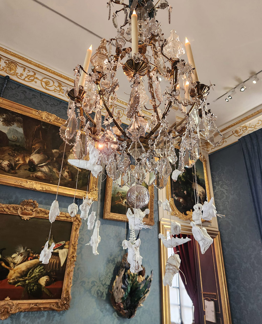 a chandelier with porcelain sculptures of animals, people and bones hanging from it