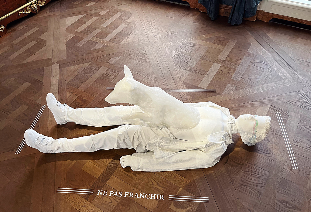 a white sculpture of a boy lying down and a fox emerging from his torso