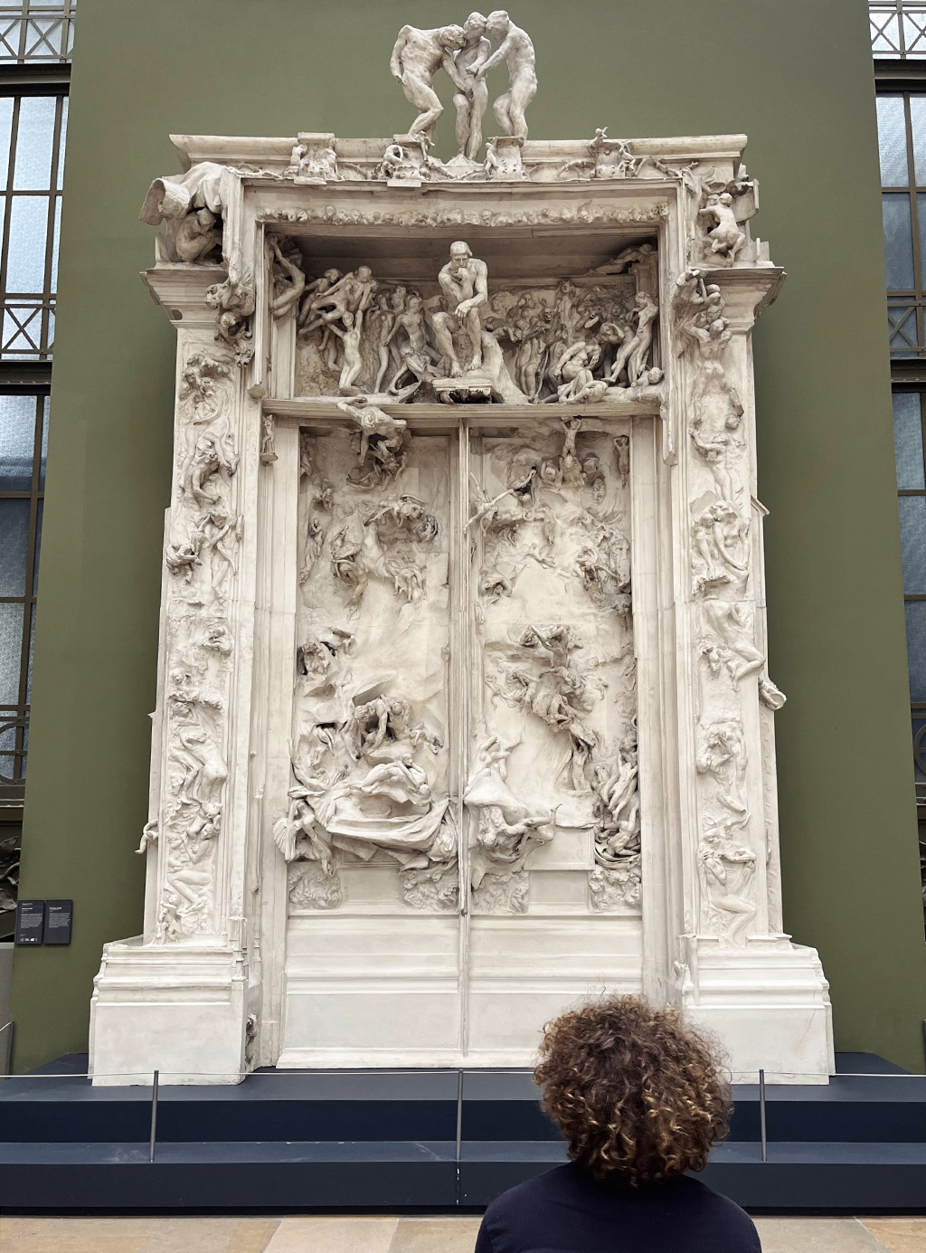 the back of the head of a curly haired man looking at a plaster model of Rodin's Gates of Hell